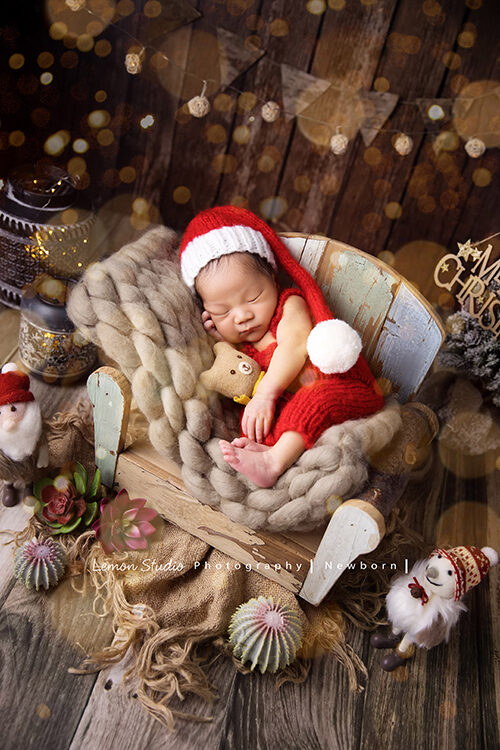 具有耶誕氛圍的專業新生兒寫真相片，這張攝影師佈置出充滿聖誕節節慶感覺的場景，戴著聖誕帽的新生兒寶寶抱著小熊睡在椅子上好可愛！