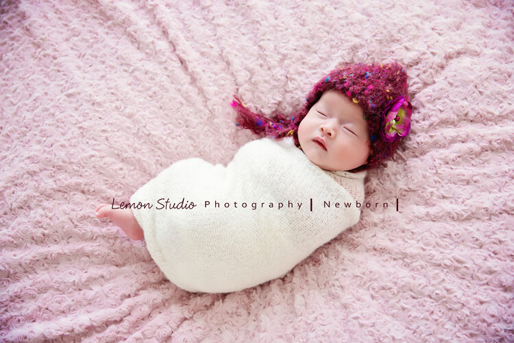 這張是隨手分享的一張新生兒攝影相片，相片裡的女寶寶帶著紫色的毛帽，包在白色的布裡，躺在粉紅色的布上，可以感覺到是一位很溫柔的女寶寶啊！