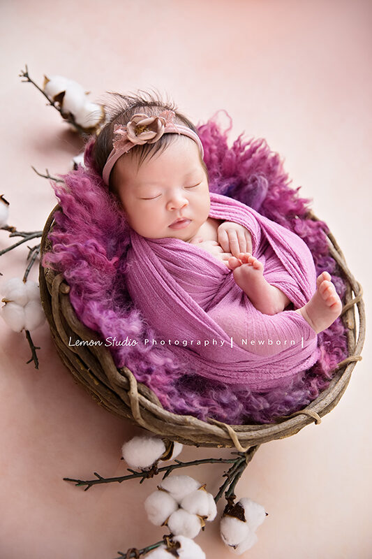 隨手分享的新生兒寶寶照，這張寶寶包在紫色的布裡，躺在紫色的毛毯及藤籃裡，好可愛啊！腳丫丫們也好有戲！