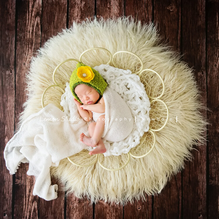 這張相片寶寶包在布裡，戴的頭套也好美，躺在花籃及地毯上好美啊！