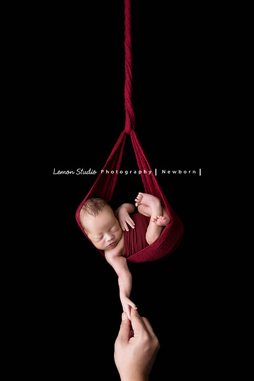 彥君媽麻一家來拍新生兒攝影，這張寶寶吊掛在紅色的布裡，爸爸牽著寶寶的一隻手，好有趣啊！