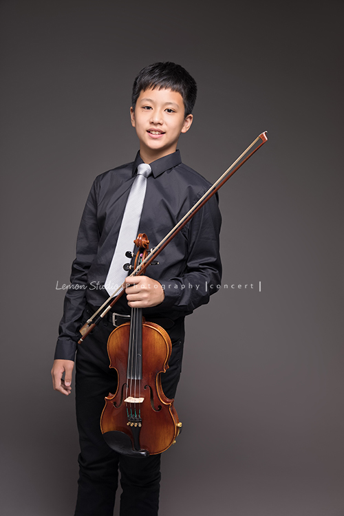 宇哲是學校弦樂團的一員，這天和團員們為了即將來到的音樂會一起來拍照，這張是宇哲手拿提琴的相片！