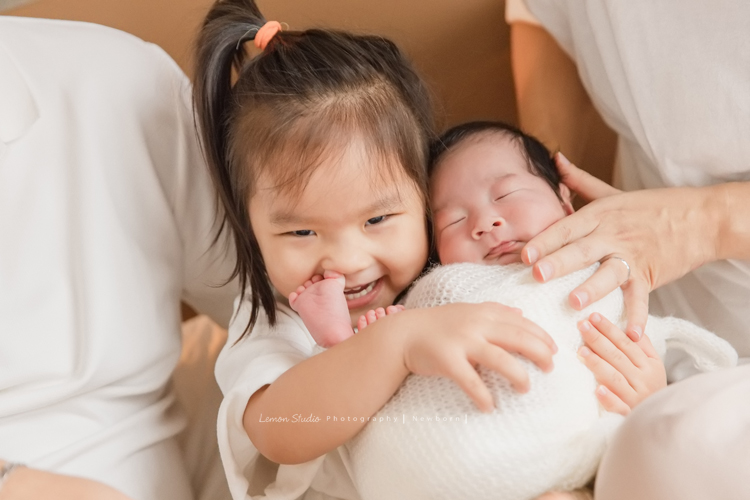 三歲的沐芯當姊姊了好開心啊，這次是拍弟弟的新生兒攝影，承錇媽麻在生產前與黎爸溝通，不用新生兒的可愛道具，希望自然感覺的拍攝，這張是小姊姊抱著睡著的弟弟，但弟弟的一隻腳在小姊姊的鼻口裡的可愛逗趣相片！