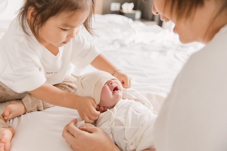 三歲的沐芯當姊姊了好開心啊，這次是拍弟弟的新生兒攝影，承錇媽麻在生產前與黎爸溝通，不用新生兒的可愛道具，希望自然感覺的拍攝，這張是小姊姊試著幫弟弟戴帽子，但弟弟在哭哭的很可愛逗趣的相片！